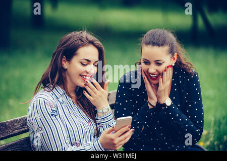 Euphoric female friends watching videos on a smartphone and surprised looking at screen. Stock Photo