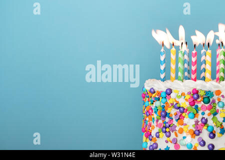 Birthday cake with lots of colorful candles and sprinkles on a blue background Stock Photo