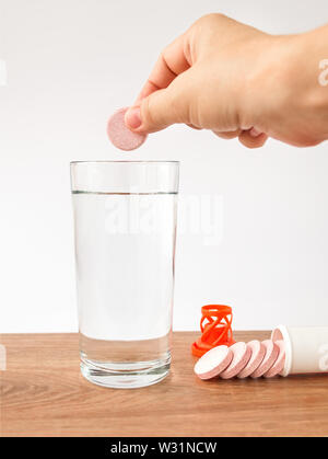 Woman hand holding soluble effervescent vitamin pill over a glass of pure drinking water. Vitamins and nutritional supplements. Healthcare and medical Stock Photo
