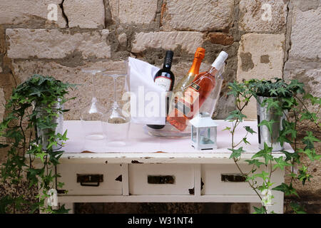 wine bottles and glasses on a side table outside  in daylight against a stone wall Stock Photo