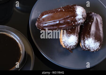 chocolate eclairs on a plate and cup of coffee. traditional fcench Chocolate Eclairs. Stock Photo