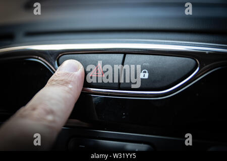 A finger pressing a hazard warning light on the interior of a car Stock Photo