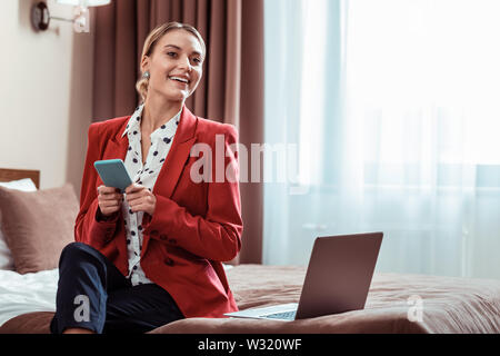 Smiling good-looking lady in a red jacket sitting on the bed Stock Photo