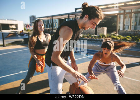 Friends playing basketball game on a sunny day on street court. Group of friends practicing basketball dribbling skills on street. Stock Photo
