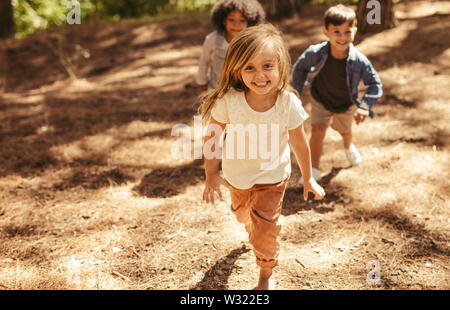 Cute girl running up hill in a park with friends. Group of kids playing together in forest. Stock Photo