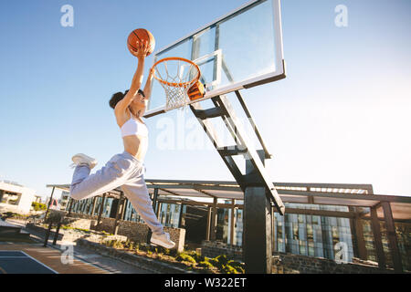 Woman basketball player slam dunking on street court. Female playing basketball outdoors on summer day. Stock Photo