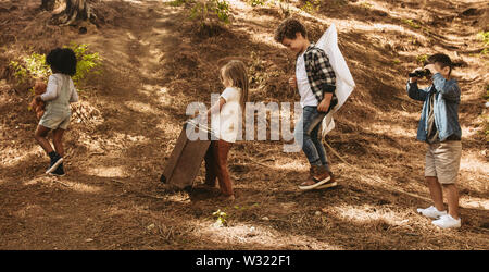 Group of children walking in the forest with their toys. Boys and girl with teddy bear, old suitcase, kite and binoculars. Stock Photo