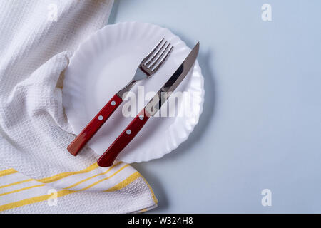 Flat lay food background with empty white plate, and cutlery, over light blue background, copy space. Stock Photo