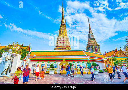 BANGKOK, THAILAND - APRIL 22, 2019: Tourists walk around large courtyard of Wat Pho religion complex, enjoy magnificent architecture surrounding build