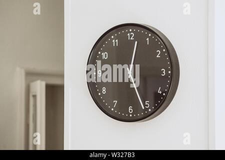 Round black clock on the white wall in the room. Detail of home interior. Stock Photo