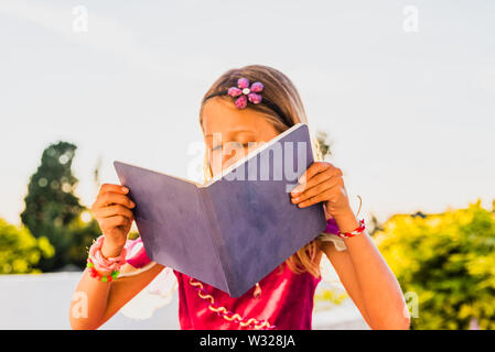 Teenage girl in princess dress disguised using her imagination to read a book outdoors. Stock Photo