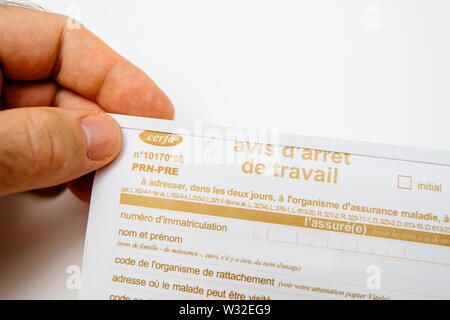 Paris, France - Jun 19, 2019: Close-up of patient male man holding above white executive table the Avis d'arret de travail Sick leave issued by treating doctor medical justification Stock Photo