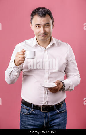 Smiling adult man with cup of coffee looking at camera against of isolated pink background. Stock Photo