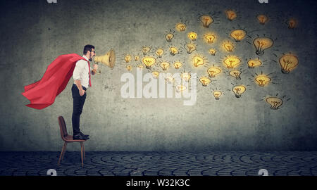 Young super hero business man standing on a chair screaming in megaphpne spreading new ideas Stock Photo