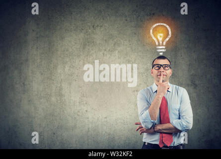 Portrait of a thinking business man looking up at bright light bulb above head Stock Photo