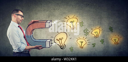 Business man attracts bright ideas light bulbs and money with a big magnet Stock Photo