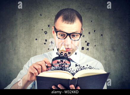Amazed man using magnifying glass reading a book with letters flying away from it Stock Photo