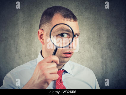 Curious young business man looking through a magnifying glass Stock Photo