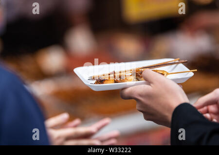Closeup of man hands holding skewered scallops on skewer stick on platter or tray in Tsukiji outer outdoor street market in Ginza, Tokyo Japan Stock Photo
