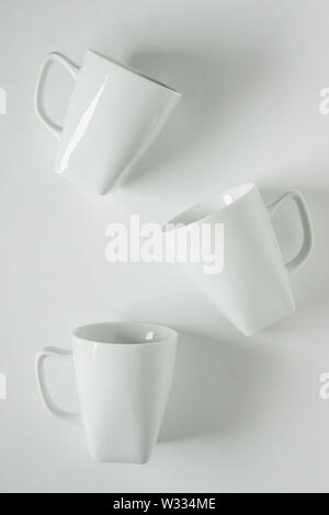 3 monochromatic white coffee mugs scattered on white background with blank empty room space for text, copy, or copy space. Modern top view concept of Stock Photo