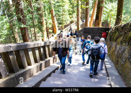 Nikko, Japan - April 4, 2019: Couple tourists, people walking on stone steps stairs up in Tochigi prefecture in mountain forest leading to Toshogu tem Stock Photo