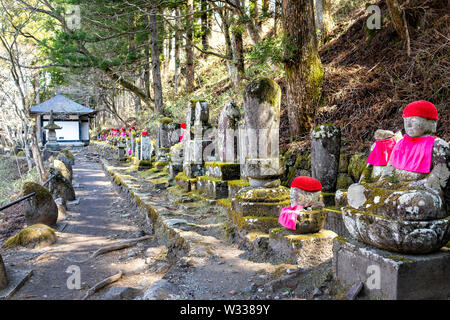 Famous stone red Jizo statues in Kanmangafuchi Abyss of Nikko, Tochigi in Japan with hats protecting the dead and temple shrine in forest Stock Photo