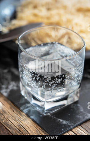 a glass of carbonated water on wooden table with a plate of out of focus pasta behind Stock Photo