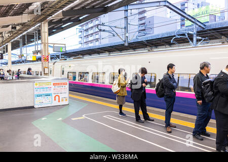 Utsunomiya, Japan - April 4, 2019: Business people, businessman and woman in suit with backpack waiting in line for arriving shinkansen bullet train t Stock Photo