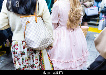 Tokyo, Japan - April 4, 2019: Back of two young women girls dressed in cosplay dolls, pink dress inside of busy Shinjuku train station terminal with p Stock Photo