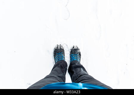 First person view of legs in hiking boots in the snow. Snow on boots while walking in winter. Stock Photo