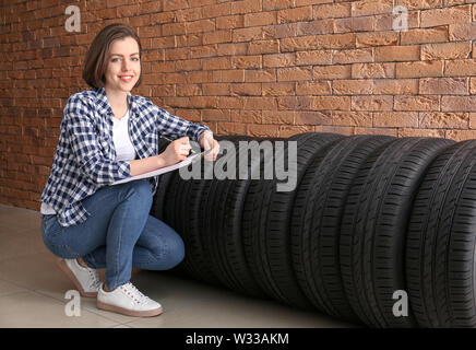 Young woman with car tires and clipboard near brick wall Stock Photo