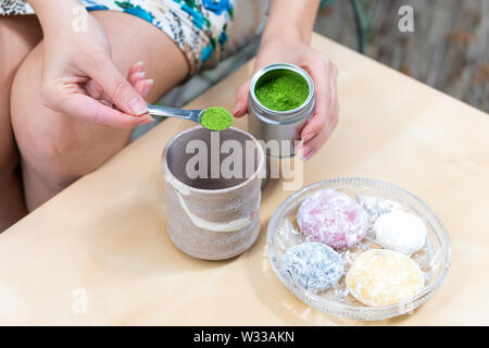 Green matcha and mochi rice cake Japanese dessert colorful daifuku with woman girl hand preparing tea powder measuring spoon on table Stock Photo