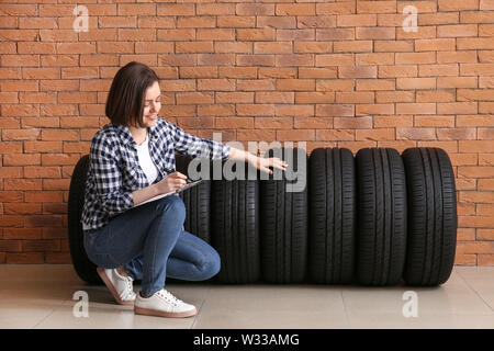 Young woman with car tires and clipboard near brick wall Stock Photo