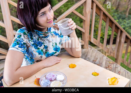 Woman with black asian hair happy smiling sitting at table holding matcha green tea cup outside in backyard garden and daifuku mochi Stock Photo