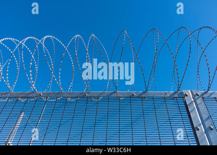 razor wire atop a security fence with deep blue sky behind Stock Photo