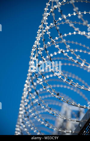 razor wire atop a security fence with deep blue sky behind Stock Photo