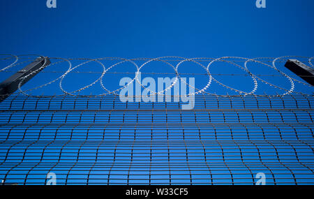 razor wire atop a security fence with deep blue sky behind Stock Photo