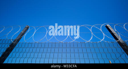 razor wire atop a security fence with deep blue sky behind Stock Photo