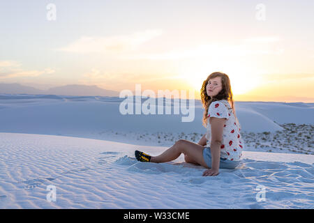 Woman girl sitting in white sands dunes national monument in New Mexico view of sunset on horizon