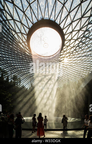 Vertical view of the waterfall with beautiful natural lighting coming into Jewel Changi Airport. Tourists and visitors taking picture, Singapore Stock Photo