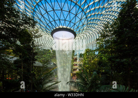 Landscape interior view of Jewel Changi Airport with blue sky and rainbow, there is also a skytrain in the back coming through the track, Singapore Stock Photo