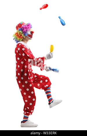 Full length profile shot of a clown juggling with clubs isolated on white background Stock Photo