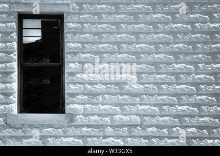 An old building made of Allen block, the texture off centers the lone dark window, in black and white, Southwest, USA, Stock Photo