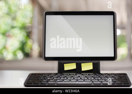 A computer with a touchscreen and wireless keyboard on a white desk with a window view in the background. Stock Photo