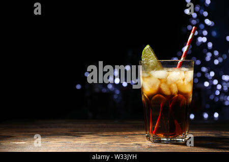 Glass with cola, lime slice and tubule against blurred lights background Stock Photo