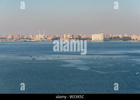 Ismailia, Egypt - November 5, 2017: Cityscape of Ismailia on the lake Timsah from ship passing Suez Canal, Ismailia, Egypt. In the foreground, fisherm Stock Photo