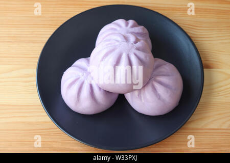 Plate of purple sweet potato steamed buns served on wooden table Stock Photo