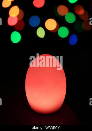 Vibrant red egg shaped table lighting with colorful bokeh in the dark Stock Photo