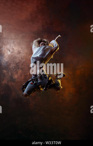 Photo of jumping long-haired blonde in torn jeans on brown background in studio Stock Photo