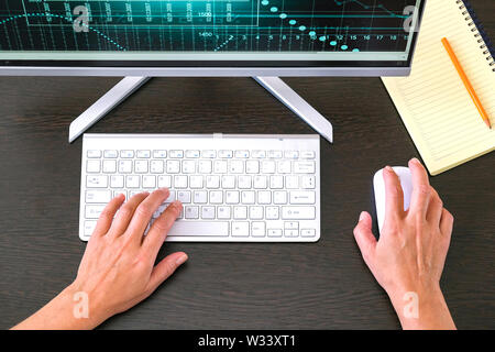 Stock chart on the monitor. Office Desk with computer and keyboard in background. Notepad and pen are prepared for work records Stock Photo
